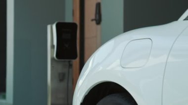 İlerici adam evindeki elektrikli aracın aküsüne emisyonsuz güç bağlantısı kuruyor. Elektrikli araç elektrik istasyonundan EV araba aküsüne kabloyla şarj oluyor.