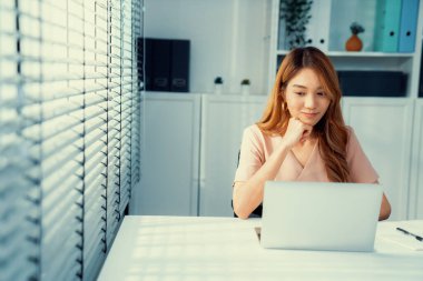 A young Asian female employee sitting at her desk in her office, sitting at desktop in workstation.