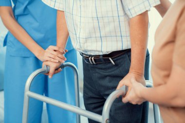 Contented senior man walking as he is helped by his wife and caretaker, walking with the aid of a folding walker. Nursing home for the elderly concept.