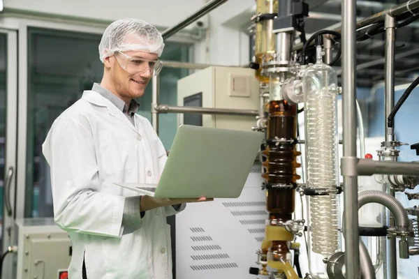 Apothecary scientist using laptop to record information from a CBD oil extractor and a scientific machine used to create medicinal cannabis products.