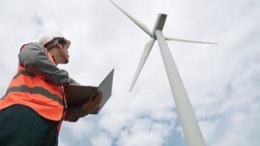 Gökyüzü arka planına sahip bir rüzgar türbini üzerinde çalışan mühendis. Yenilenebilir ve sürdürülebilir enerjinin gelecekteki üretimi için yenilikçi bir ideal. Rüzgar türbininden enerji üretimi.