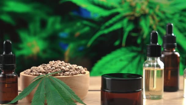 大麻合法研究所で生産された天然スキンケア化粧品モックアップ製品 大麻植物の背景の庭とテーブルの上のCbd油 麻種子 および保湿クリームジャー製品 コピースペース — ストック動画