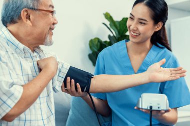 A contented retired man having a blood pressure check by his personal caregiver at his home with a smiley face. Senior care at home, nursing home for pensioners.