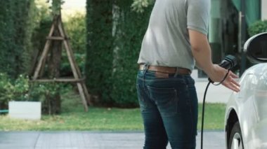 İlerici adam evindeki elektrikli aracın aküsüne emisyonsuz güç bağlantısı kuruyor. Elektrikli araç elektrik istasyonundan EV araba aküsüne kabloyla şarj oluyor.