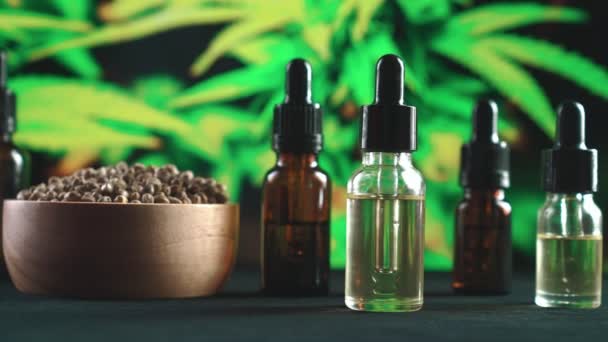 大麻植物 麻の葉から合法化されたマリファナ製品 様々なサイズのCbdオイルボトル 大麻植物の背景を持つテーブルの上に麻の葉を持つ麻の種の木製のボウルコピースペース — ストック動画