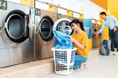 Asian people using qualified coin operated laundry machine in the public room to wash their cloths. Concept of a self service commercial laundry and drying machine in a public room. clipart