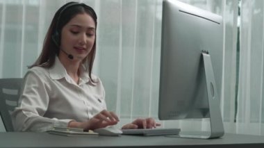 Masasında dizüstü bilgisayarla çalışan kulaklık ve mikrofon takan Asyalı müşteri destek operatörü. Hevesli kadın çalışanlar müşteri hizmetleri sunuyor, destekleyici çağrı merkezi temsilcisi müşterilere yardım ediyor.