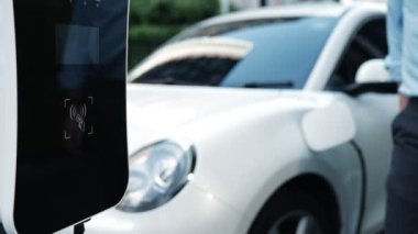 Bir adam kredi kartını, şarj istasyonundaki elektrikli aracının temiz ve sürdürülebilir enerjisini ödemek için kullanıyor. Yenilikçi adam şarj edilebilir aracına güç sağlamak için ödeme yapıyor..