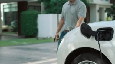 İlerici adam evindeki elektrikli aracın aküsüne emisyonsuz güç bağlantısı kuruyor. Elektrikli araç elektrik istasyonundan EV araba aküsüne kabloyla şarj oluyor.
