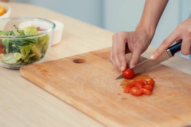 Close up hands holding a knife preparing a contented meal. Sliced tomatoes and other vegetables on the glass dish.