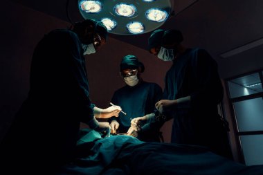 Steril ameliyathanedeki hastaya ameliyat yapan cerrahi ekip. Bir lambanın yaktığı ameliyathanede, profesyonel ve kendinden emin bir cerrahi ekip bilinçsiz bir hastaya tıbbi bakım sağlar..