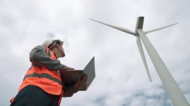 Gökyüzü arka planına sahip bir rüzgar türbini üzerinde çalışan mühendis. Yenilenebilir ve sürdürülebilir enerjinin gelecekteki üretimi için yenilikçi bir ideal. Rüzgar türbininden enerji üretimi.