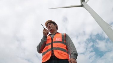 Gökyüzü arka planına sahip bir rüzgar türbini üzerinde çalışan mühendis. Yenilenebilir ve sürdürülebilir enerjinin gelecekteki üretimi için yenilikçi bir ideal. Rüzgar türbininden enerji üretimi.