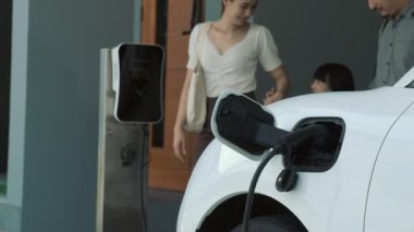 İlerici ebeveynler kızlarını okuldan alırken elektrikli araba ve yenilenebilir enerji kavramını kullandılar, evdeki EV otomobil için şarj istasyonu. Alternatif eko taşımacılığı.
