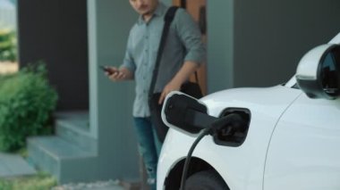 Adamın biri evinde elektrikli araç şarj aletinin fişini çekiyor. İlerici bir yaşam tarzında elektrikli araçların kullanımı, temiz ve sağlıklı bir çevreye katkıda bulunur..