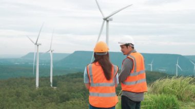 Erkek ve kadın mühendisler kırsal kesimdeki bir tepenin tepesinde ya da dağda rüzgar çiftliğinde çalışıyorlar. Yenilenebilir ve sürdürülebilir enerjinin gelecekteki üretimi için yenilikçi idealler.