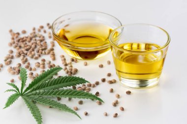 CBD yağı, cam kasede THC tintürü, damlalık kapaklı şişe ve boş arka planda kenevir yaprağı minimalizmle çevrili bir yığın kuru kenevir tohumu. Yasal marihuana konsepti.