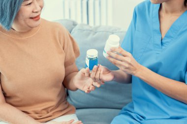 Caregiver advising contented senior woman on medication in the living room. Medication for seniors, nursing house, healthcare at home.