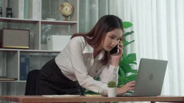 Genç hevesli iş kadını iş görüşmesinde konuşuyor ve masasına dizüstü bilgisayarla bir not yazıyor. Kadın çalışan telefonda konuşuyor ve ofis evraklarına iş ödevi yazıyor..