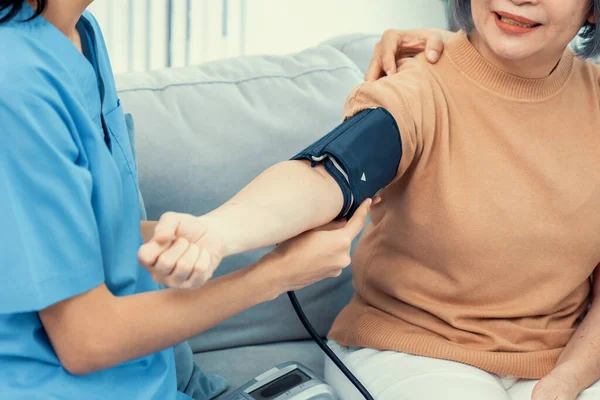 An elderly woman with a contented life having a blood pressure check by her caregiver at home with a smiley face.