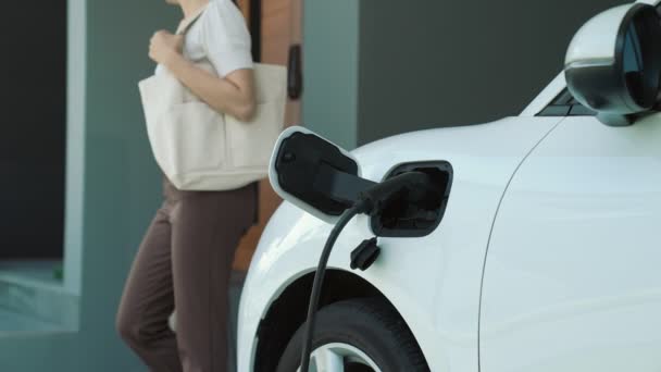 女性が電気自動車の充電器を彼の家に取り外します 先進的なライフスタイルにおける電気自動車の使用の概念は 清潔で健康的な環境に貢献します — ストック動画