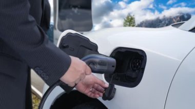 İş dünyasındaki yenilikçi adam elektrikli arabasını dağlarla dolu bir kırsal kesimdeki şarj istasyonundan alıyor. Yol yolculuğu, EV arabalı macera yenilenebilir enerjiyle çalışıyor..