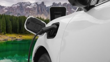 Temiz çevre için temiz enerjinin yol açtığı ilerici elektrikli araba kavramının arka planı olarak dağın tepesinde bulutun zaman kavramının yer aldığı doğal manzara. EV araba şarj istasyonunda şarj oluyor..