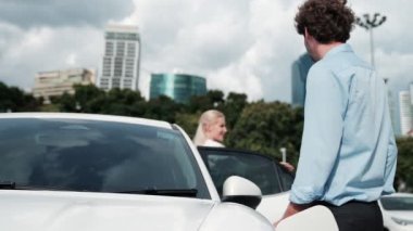 İlerici iş adamı ve iş kadını şehir merkezinde dolaşmadan önce şarj istasyonuna bağlı elektrikli arabaya yaslanıyor. Çevre dostu şarj edilebilir araba temiz enerjiyle çalışıyor..