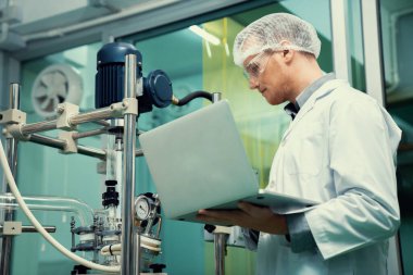 CBD yağ çıkarıcısının yanında dizüstü bilgisayarla çalışan eczacı bilim adamı ve tıbbi esrar ürünleri üretmek için kullanılan bilimsel bir makine.