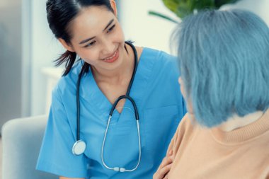 A caregiver rest her hands on the shoulders of a contented senior patient while she sitting on the sofa at home.
