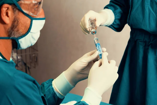 stock image Surgeon fill syringe from medical vial for surgical procedure at sterile operation room with assistance nurse. Doctor and medical staff in full protective wear for surgery prepare anesthesia injection