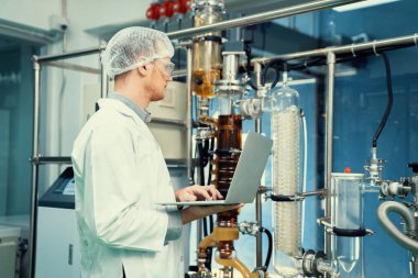 CBD yağ çıkarıcısının yanında dizüstü bilgisayarla çalışan eczacı bilim adamı ve tıbbi esrar ürünleri üretmek için kullanılan bilimsel bir makine.