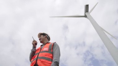 Gökyüzü arka planına sahip bir rüzgar türbini üzerinde çalışan mühendis. Yenilenebilir ve sürdürülebilir enerjinin gelecekteki üretimi için yenilikçi bir ideal. Rüzgar türbininden enerji üretimi.