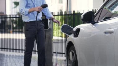 İlerici işadamı, şehir merkezinde dolaşmadan önce şarj cihazından elektrikli arabasına şarj prizi takıyor. Çevre dostu şarj edilebilir araba, sürdürülebilir ve temiz enerjiyle çalışıyor..