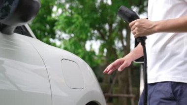 İlerici adam elektrikli aracına elektrik kablosu takıyor. Ev şarj istasyonundan EV arabası. Çevreyi korumak için temiz ve yenilenebilir enerji kullanan elektrikli bir araba. Çevre dostu otomobil.