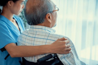 Rear view of a caregiver and her contented senior patient gazing out through the window. Elderly illness, nursing homes for the elderly, and pensioner life