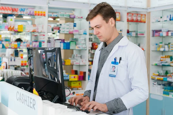 Portrait of male pharmacist using computer checking medicine or medical supply storage at counter in pharmacy. Inventory work in qualified chemist shop drugstore concept.