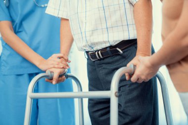 Contented senior man walking as he is helped by his wife and caretaker, walking with the aid of a folding walker. Nursing home for the elderly concept.