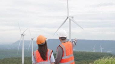 Erkek ve kadın mühendisler kırsal kesimdeki bir tepenin tepesinde ya da dağda rüzgar çiftliğinde çalışıyorlar. Yenilenebilir ve sürdürülebilir enerjinin gelecekteki üretimi için yenilikçi idealler.