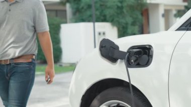 İlerici adam evindeki elektrikli aracın aküsüne emisyonsuz güç bağlantısı kuruyor. Elektrikli araç elektrik istasyonundan EV araba aküsüne kabloyla şarj oluyor.