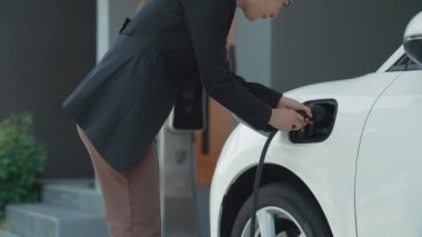 Bir kadın evinde elektrikli araç şarj aletinin fişini çekiyor. İlerici bir yaşam tarzında elektrikli araçların kullanımı, temiz ve sağlıklı bir çevreye katkıda bulunur..