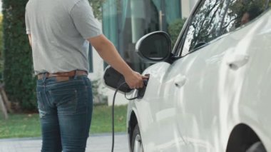 Adamın biri evinde elektrikli araç şarj aletinin fişini çekiyor. İlerici bir yaşam tarzında elektrikli araçların kullanımı, temiz ve sağlıklı bir çevreye katkıda bulunur..