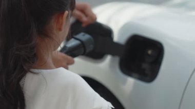 İlerici baba-kız elektrikli araç şarj istasyonundan fiş takıyor. Geleceğin çevre dostu arabası yenilenebilir temiz enerji kaynağıyla çalışıyor..