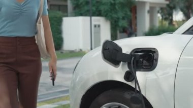 Evinde şarj edilen elektrikli bir araçla işten yeni dönen modern bir kadının ilerici yaşam tarzı. Elektrikli araç, sürdürülebilir temiz enerjiyle çalışıyor..