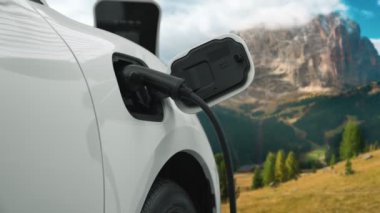 Temiz çevre için temiz enerjinin yol açtığı ilerici elektrikli araba kavramının arka planı olarak dağın tepesinde bulutun zaman kavramının yer aldığı doğal manzara. EV araba şarj istasyonunda şarj oluyor..