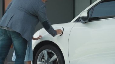 İlerici baba-kız elektrikli araç şarj istasyonundan fiş takıyor. Geleceğin çevre dostu arabası yenilenebilir temiz enerji kaynağıyla çalışıyor..