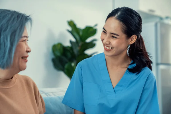 stock image A caregiver rest her hands on the shoulders of a contented senior patient while she sitting on the sofa at home.