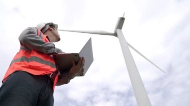Gökyüzü arka planına sahip bir rüzgar türbini üzerinde çalışan mühendis. Yenilenebilir ve sürdürülebilir enerjinin gelecekteki üretimi için yenilikçi bir ideal. Rüzgar türbininden enerji üretimi.
