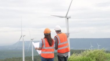 Erkek ve kadın mühendisler kırsal kesimdeki bir tepenin tepesinde ya da dağda rüzgar çiftliğinde çalışıyorlar. Yenilenebilir ve sürdürülebilir enerjinin gelecekteki üretimi için yenilikçi idealler.