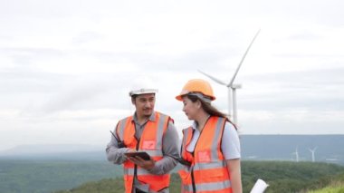 Erkek ve kadın mühendisler kırsal kesimdeki bir tepenin tepesinde ya da dağda rüzgar çiftliğinde çalışıyorlar. Yenilenebilir ve sürdürülebilir enerjinin gelecekteki üretimi için yenilikçi idealler.